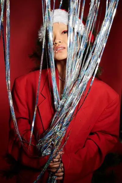 A beautiful Asian woman in a vibrant red outfit embraces festive decorations while smiling warmly. — Stock Photo