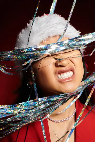 A radiant Asian woman playfully embraces the holiday cheer with sparkling decorations around her. — Stock Photo