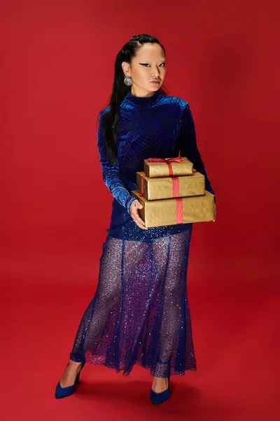 Dressed in a dazzling blue gown, she elegantly presents three wrapped gifts in a festive setting. — Stock Photo