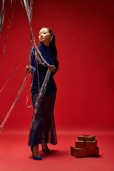 A fashionable woman in a shimmering outfit holds shimmering strings, surrounded by gifts. — Stock Photo