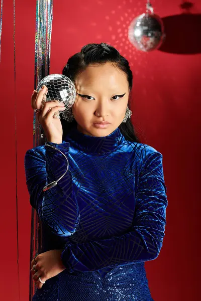 A confident Asian woman flaunts her style with a disco ball amidst sparkling glitter. — Stock Photo