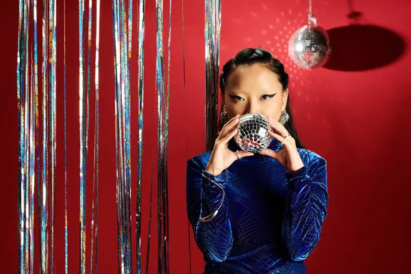 A stylish Asian woman elegantly poses with a sparkling disco ball amid shimmering decor. — Photo de stock