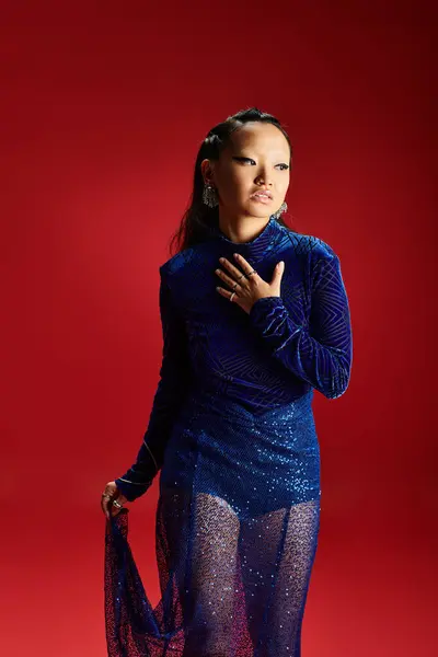 Ошеломляющая азиатка демонстрирует элегантность в блестящем синем наряде, источая уверенность и изящество. — стоковое фото