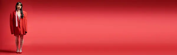 Una mujer asiática elegante ostenta un atuendo rojo de gran tamaño contra un telón de fondo audaz. — Stock Photo
