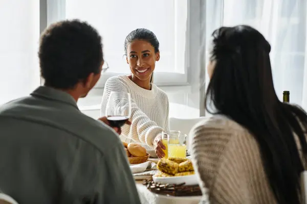 Los amigos se reúnen alrededor de una mesa bellamente puesta, disfrutando de platos y bebidas de Acción de Gracias. - foto de stock