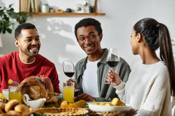 Three friends toast with glasses while enjoying a heartwarming Thanksgiving meal at home. — Stock Photo