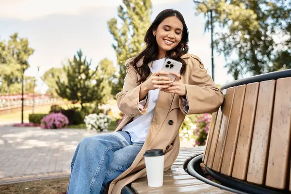 She relaxes on a bench, dressed warmly for autumn, with a coffee cup by her side. — Stock Photo