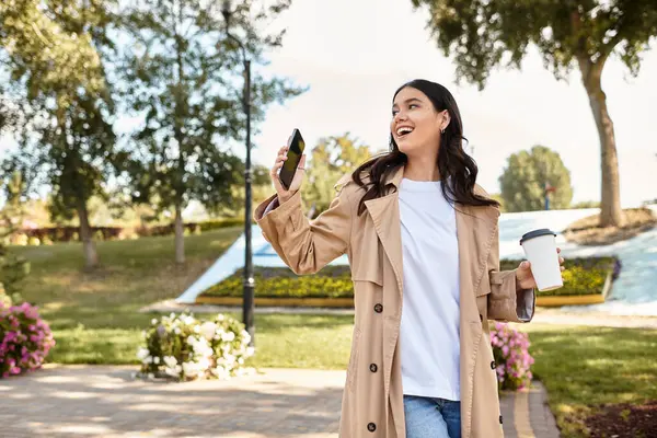 A joyful woman dressed for autumn strolls through a vibrant park, sipping coffee and smiling. — Stock Photo
