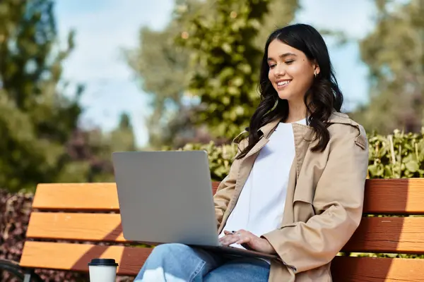 A young woman sits on a bench in a vibrant park autumn, focused on her laptop screen. — Stock Photo