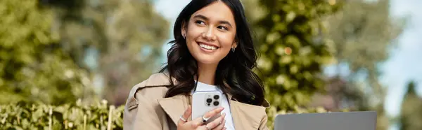 A young woman relaxes in a park, cozy in autumn clothes and using her devices. — Stock Photo