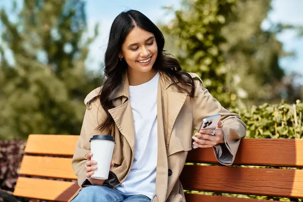 A young, beautiful woman in cozy fall attire smiles while checking her phone, surrounded by nature. — Stock Photo