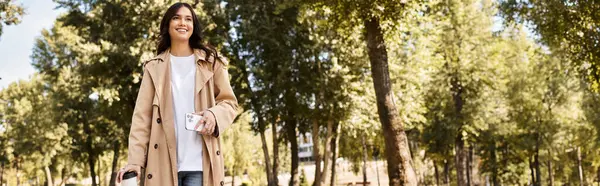 A beautiful young woman in cozy autumn attire strolls through a scenic park filled with trees. — Stock Photo