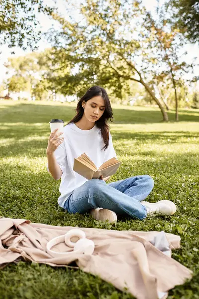 A young woman reads intently while sipping coffee in a tranquil park during autumn. — Stock Photo