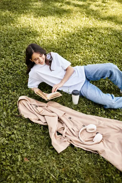 A young woman relaxes on the grass, reading a book while sipping coffee in autumn warmth. — Stock Photo