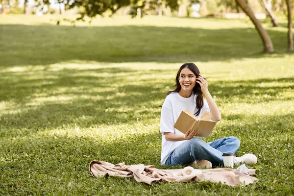 Wearing warm attire, a cheerful woman relaxes on a blanket while reading outdoors. — Stock Photo