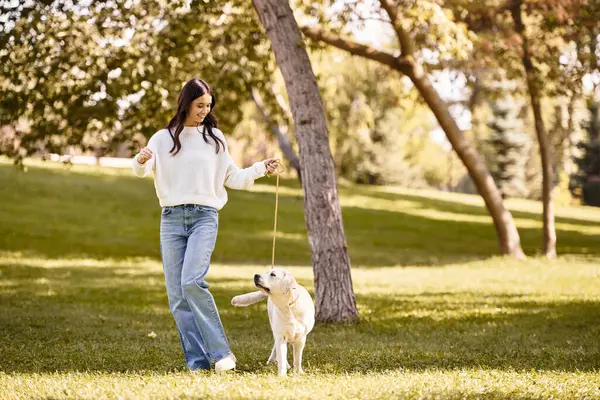 A young woman in autumn clothes walks her dog in a colorful fall park. — Stock Photo