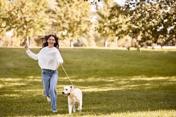 A young woman with long hair runs happily through a park with her playful dog on a sunny autumn day. — Stock Photo