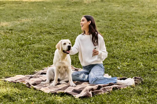 In a warm autumn outfit, a woman relaxes in the park, playing with her cheerful dog on a blanket. — Stock Photo