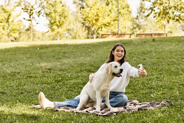 A young woman enjoys a sunny autumn day in the park while taking a selfie with her dog. — Stock Photo