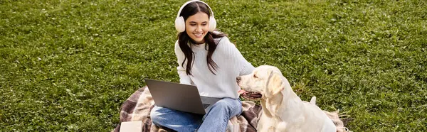 Wrapped in a warm sweater, a young woman smiles while studying outdoors with her playful dog nearby. — Stock Photo