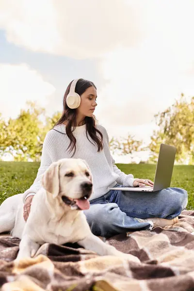 A young woman works on her laptop outdoors with her loyal dog beside her in autumn colors. — Stock Photo
