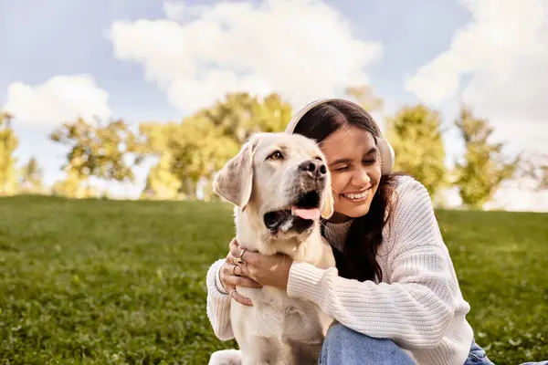 Eine junge Frau, in warme Herbstkleidung gehüllt, umarmt ihren Hund beim Entspannen im Park. — Stockfoto