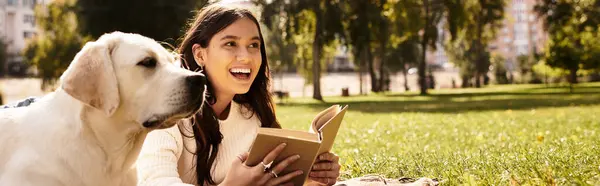 Delighting in her book, a woman sits on the grass with her dog on a beautiful autumn day. — Stock Photo