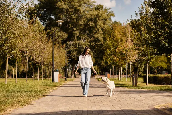 A beautiful woman in warm autumn clothing strolls through a peaceful park with her dog. — Stock Photo