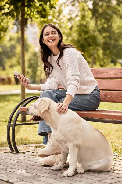 Eine junge Frau in gemütlicher Herbstkleidung entspannt sich auf einer Bank und lächelt, während sie ihren Hund streichelt. — Stockfoto
