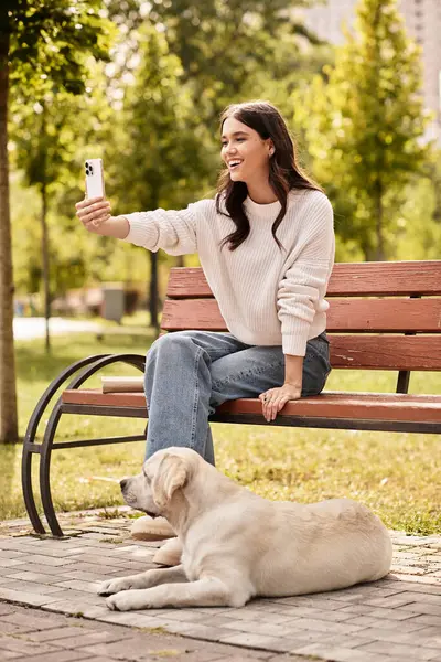 A cheerful woman enjoys a delightful moment, capturing a selfie with her loyal dog in the park. — Stock Photo