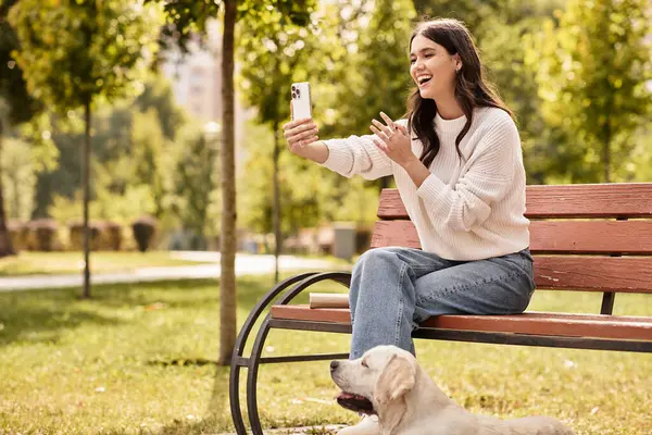A young woman in cozy autumn attire smiles as she chats on her phone, seated in a park. — Stock Photo