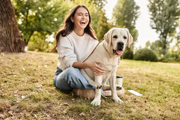 Una donna allegra in accogliente abbigliamento autunnale ride mentre gioca con il suo cane in un bel parco. — Foto stock