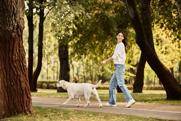 A young woman enjoys a lively walk with her dog on a beautiful autumn day in the park. — Stock Photo
