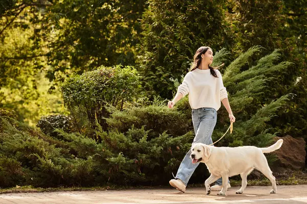 Eine junge Frau in kuscheliger Herbstkleidung geht fröhlich mit ihrem glücklichen Hund inmitten fallender Blätter spazieren. — Stockfoto