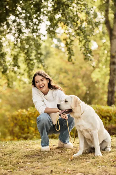 A young woman enjoys a vibrant autumn afternoon, smiling with her dog in the park. — Stock Photo