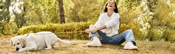 A young woman enjoys a sunny autumn day, laughing while playing with her dog in the park. — стоковое фото