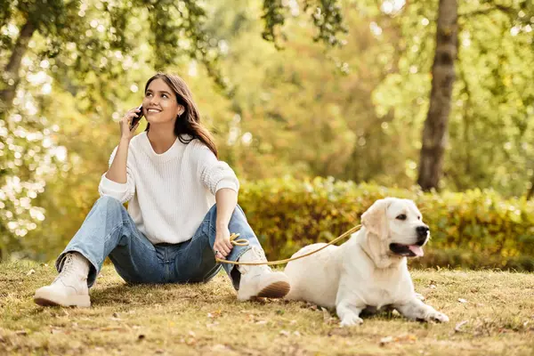 A young woman dressed in cozy autumn attire relaxes outdoors, chatting happily on her phone. — Stock Photo