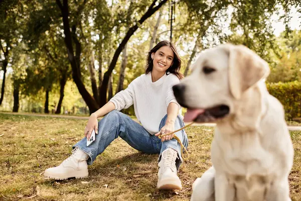 Die Frau sitzt auf dem Rasen in einem Park, lächelt und genießt das schöne Herbstwetter. — Stockfoto