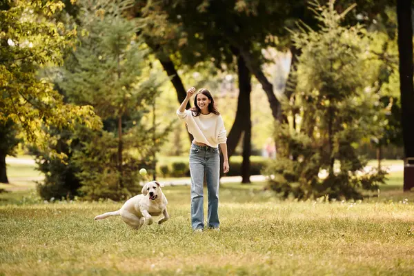 A joyful woman wears cozy autumn attire while frolicking with her dog in a leafy park. — Stock Photo