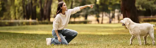 A young woman in cozy autumn clothes plays with her dog in a sunlit park, sharing a happy moment. — Stock Photo