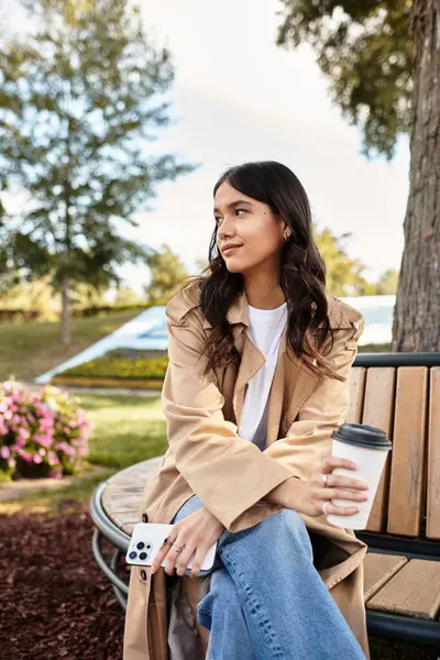 Wrapped in warm autumn layers, a young woman savors a cozy moment outdoors in a park. — Stock Photo