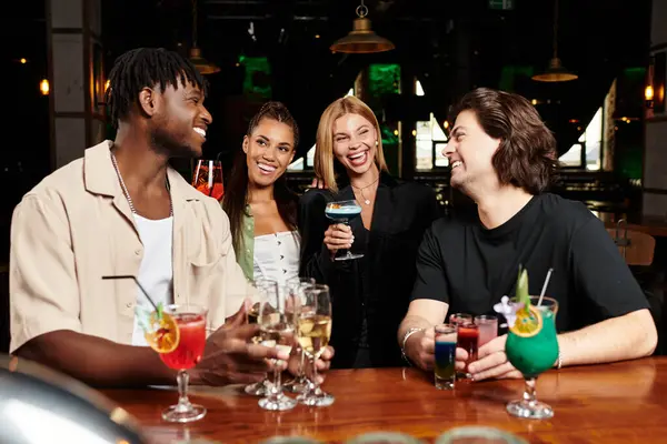 Colleagues toast with colorful cocktails while exchanging lively banter at a fun gathering. — Stock Photo