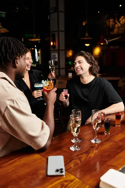 A diverse group of young colleagues enjoys drinks and laughter at a corporate celebration in a bar. — Stock Photo