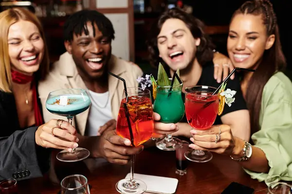 A joyous group of young colleagues raises colorful cocktails, celebrating their success at a party. — Stock Photo
