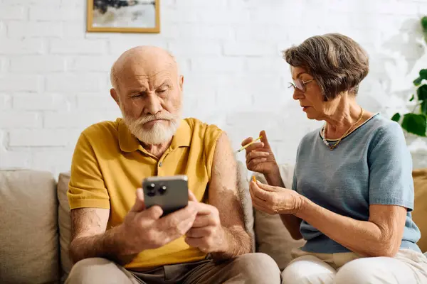 A supportive wife helps her husband manage diabetes as he uses his smartphone. — Stock Photo