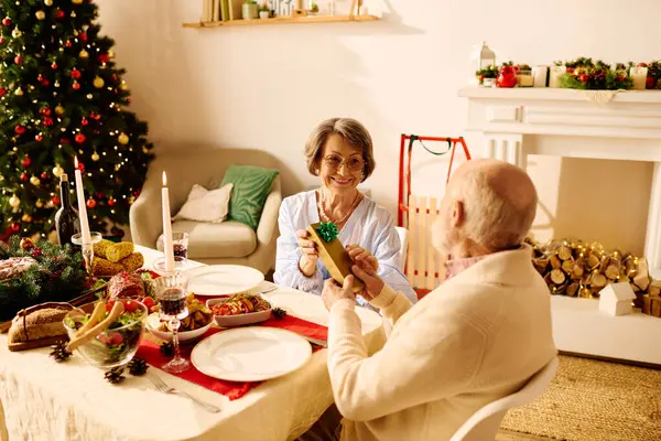 A cheerful couple exchanges presents at home, surrounded by festive holiday decorations and warmth. — Stock Photo