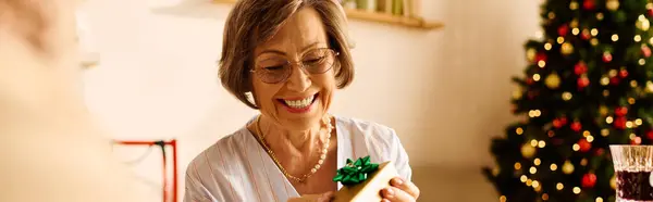 A senior woman beams as she unwraps a gift, surrounded by holiday decorations. — Stock Photo