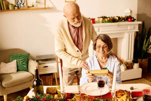 Una amante pareja de personas mayores disfruta de un momento festivo de Navidad en casa, abriendo regalos y sonriendo. - foto de stock