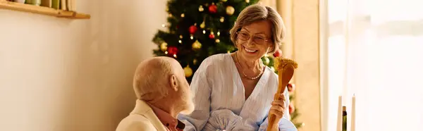 Um casal sênior celebra alegremente o Natal em casa em meio a decorações festivas. — Fotografia de Stock