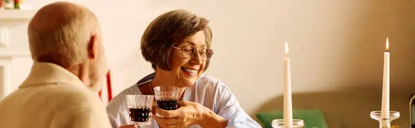 Una adorable pareja de ancianos brindando con copas de vino tinto en un acogedor entorno navideño. - foto de stock